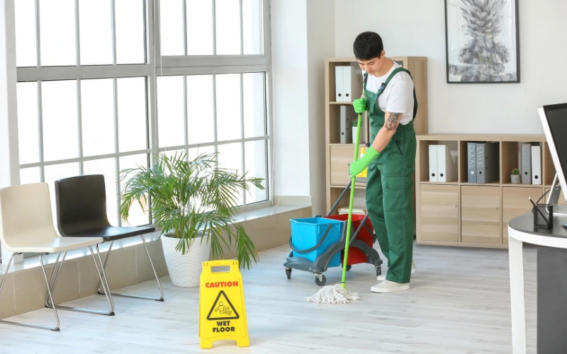 A man holding mopping stick and cleaning the floor with clear sign board