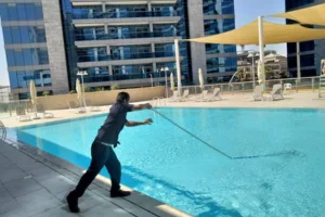 person holding the stick and removing the dust in swimming pool